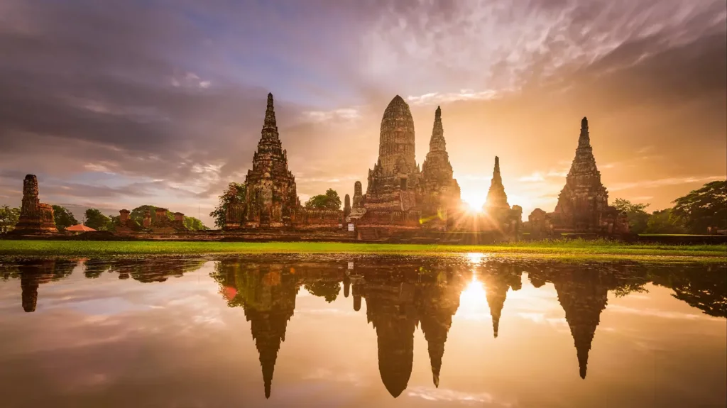 Wat Chaiwatthanaram temple complex in Ayutthaya at sunset, with ancient prangs and ruins perfectly reflected in the flooded grounds
