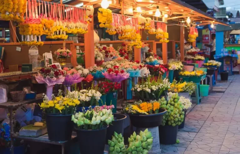 Bangkok Flower Markets: Bangkok flower market featuring vibrant fresh flowers arranged in buckets along the walkway, with golden marigold garlands suspended from the covered stall