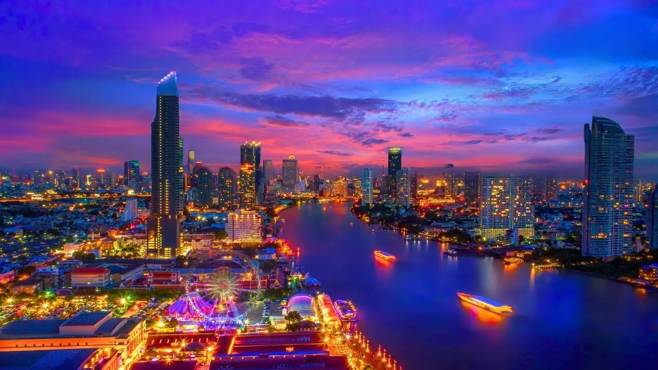 Best Things to Do in Bangkok: Spectacular evening cityscape of Bangkok featuring the iconic skyline with towering skyscrapers, colorful sunset sky, and the Chao Phraya River reflecting the city lights, with Asiatique and other landmarks visible along the waterfront