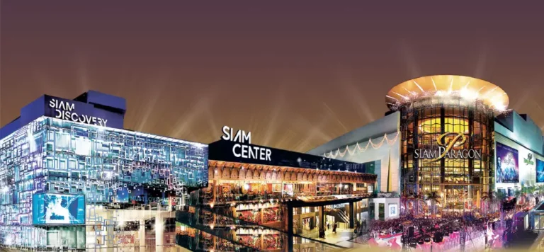 Escape the rain in Bangkok malls: Siam Paragon and Siam Discovery malls lit up at night with large crowds in the courtyard area