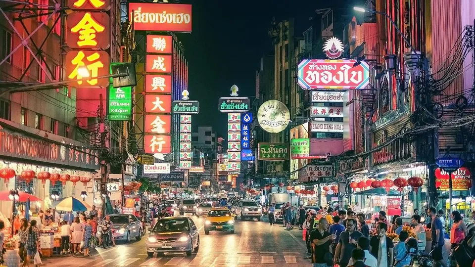 Vibrant neon signs and bustling street life in Bangkok's Chinatown at night, with families exploring the colorful shops and street food stalls