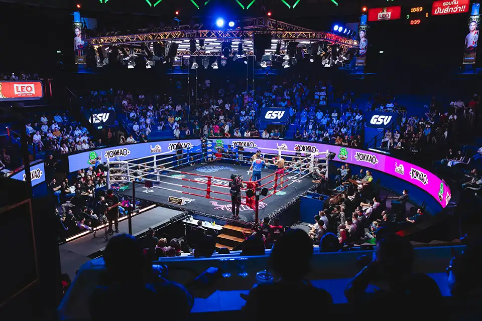 Top 10 Must-Do Activities in Bangkok: Overhead shot of fighters competing in the brightly lit boxing ring at Rajadamnern Stadium while spectators fill the tiered seating around them