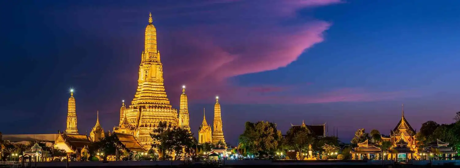 Top Photo Spots Bangkok: Spectacular evening shot of Wat Arun temple complex with its towering central spire and smaller prangs glowing golden against a dramatic purple and pink sunset sky over Bangkok