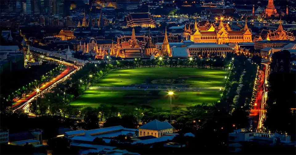 Evening at Sanam Luang: glowing palace spires, soft park lights, and urban energy all around.