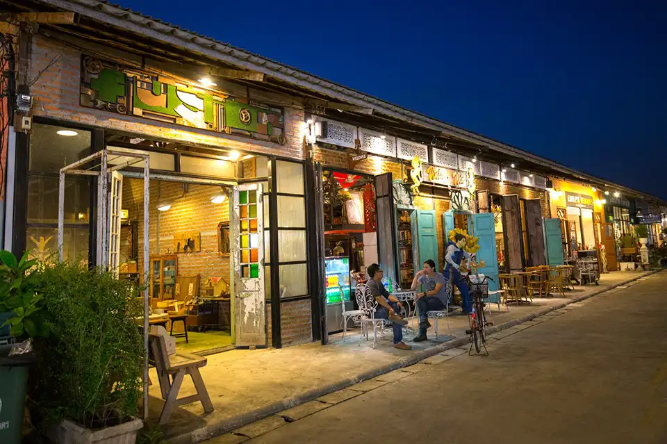 Evening at Train Night Market Srinakarin: brick walls, quirky signs, and casual street charm.