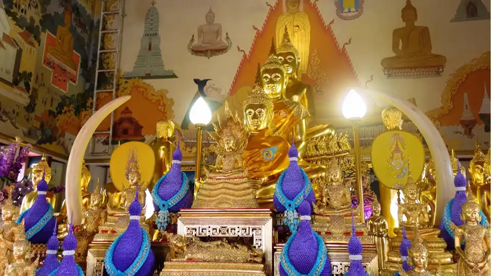 Richly decorated shrine inside Wat Intharawihan with tiered golden Buddha statues, ivory tusks, and blue-purple ceremonial decorations