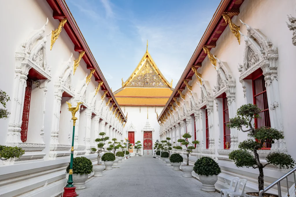The peaceful courtyard of Wat Mahathat Yuwaratrangsarit, showing the temple's elegant white architecture and golden central chapel