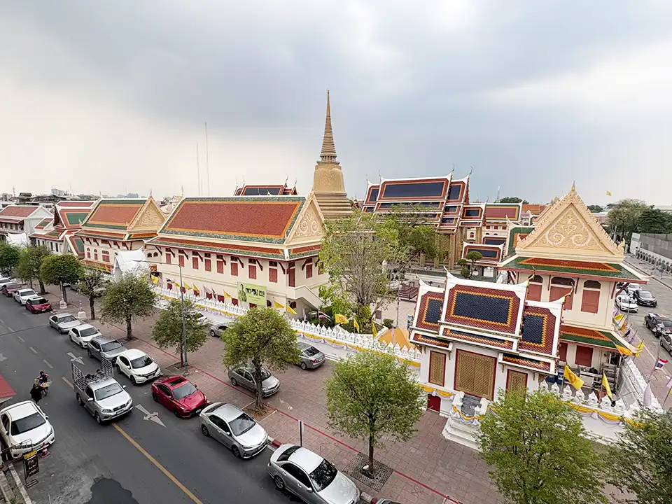 Overhead view of Wat Ratchabophit temple showing its ornate buildings with red-tiled roofs and golden spire, surrounded by parked cars and street trees