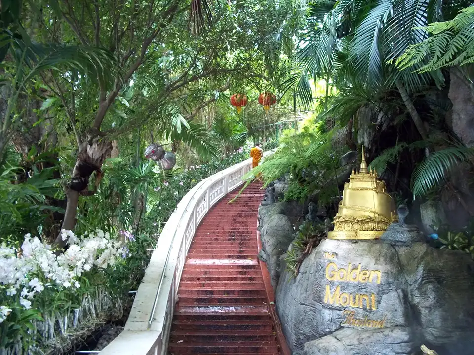 The scenic climb to Golden Mount's temple, with red stairs winding through greenery and a monk in orange robes ascending
