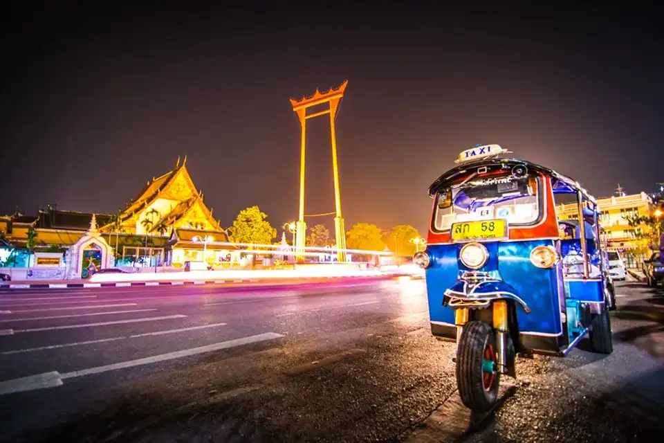 A classic blue tuk-tuk parked near Bangkok’s Giant Swing, glowing under city lights.