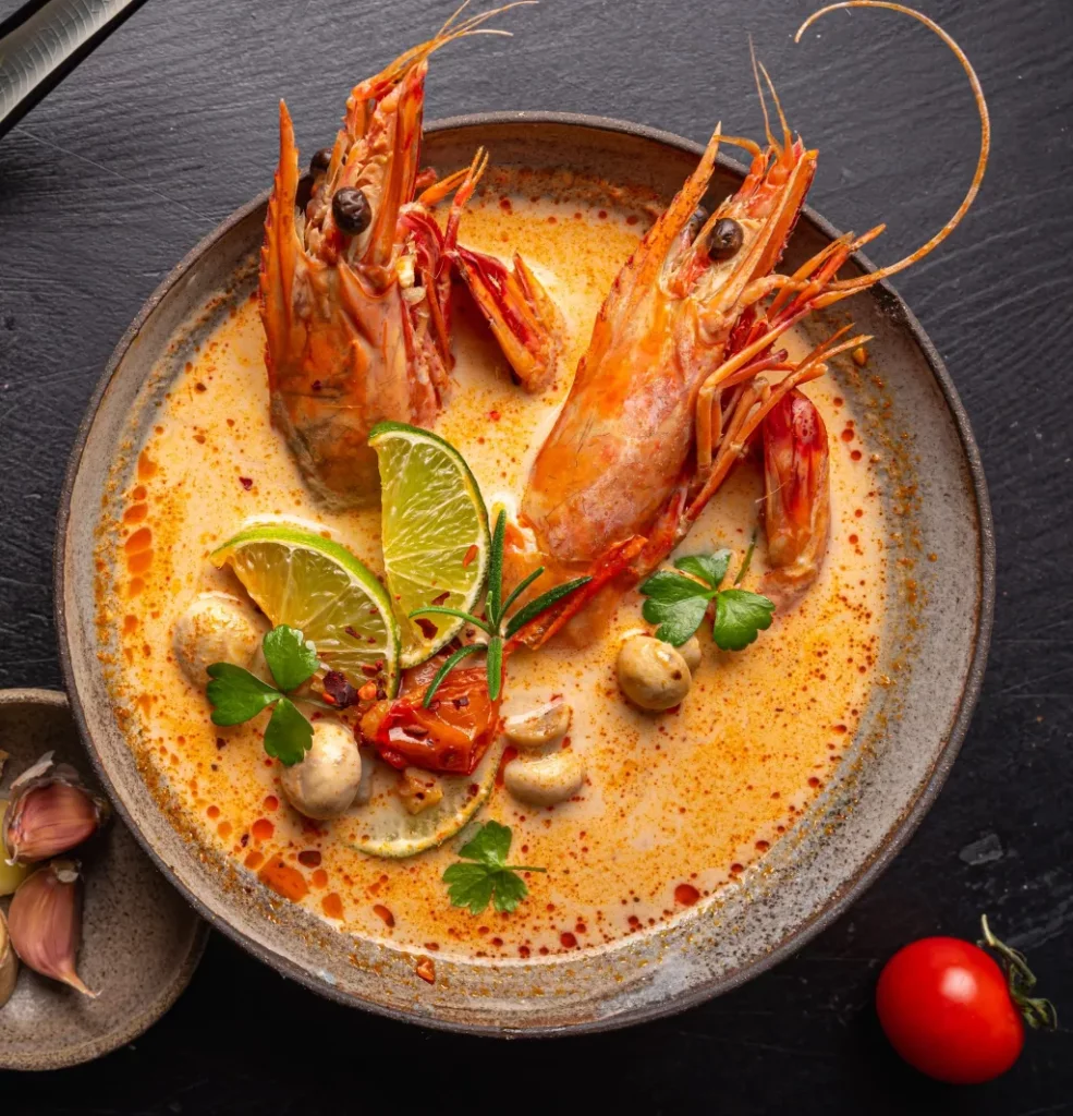 Bangkok FAQs: A steaming bowl of Tom Yum Koong with prawns, mushrooms, lime, and chili in a rich, spicy broth.
