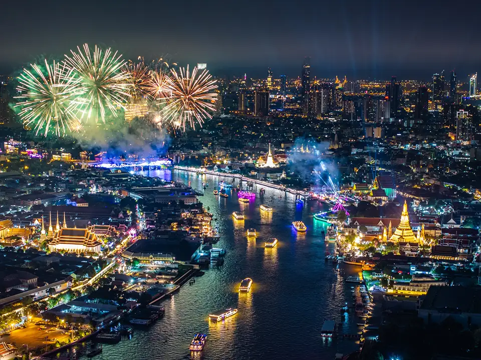 Spectacular fireworks display above the illuminated Chao Phraya River with decorated boats and lit temples along both banks during Vijit Chao Phraya 2025