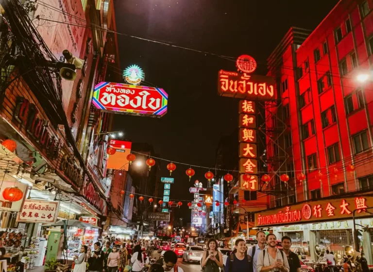 Crowded street filled with visitors who explore Chinatown in Bangkok at night, featuring colorful Thai-Chinese signage and traditional red lanterns