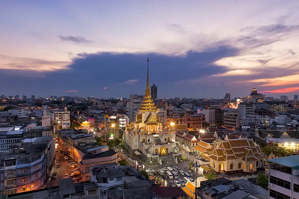 Illuminated Wat Traimit temple at dusk with its distinctive golden pagoda, a landmark to explore Chinatown in Bangkok