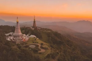 Chiang Mai photo spots: Breathtaking sunrise scene showing the famous twin chedis at Thailand's highest peak, with rolling mountains fading into the distance under a warm orange sky
