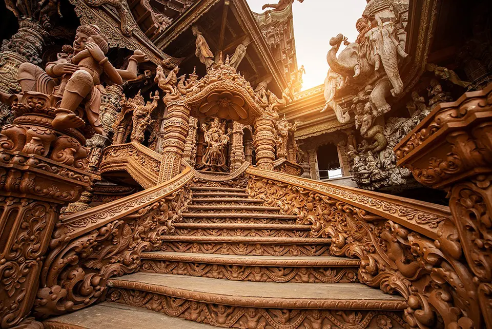 Pattaya photo spots: Close-up of the spectacular wooden craftsmanship at Pattaya's Sanctuary of Truth temple, showing intricate carved figures, elephants, and ornate Thai architectural details bathed in golden sunlight