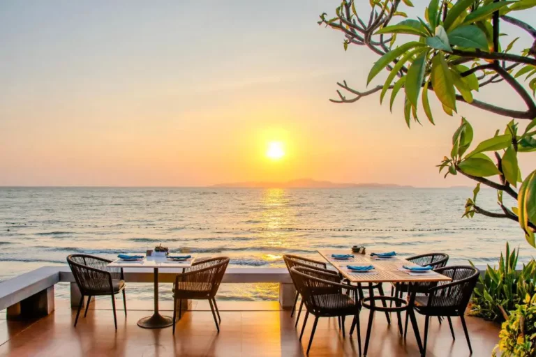 Outdoor restaurant terrace in Pattaya with wicker chairs and tables overlooking the ocean at golden hour