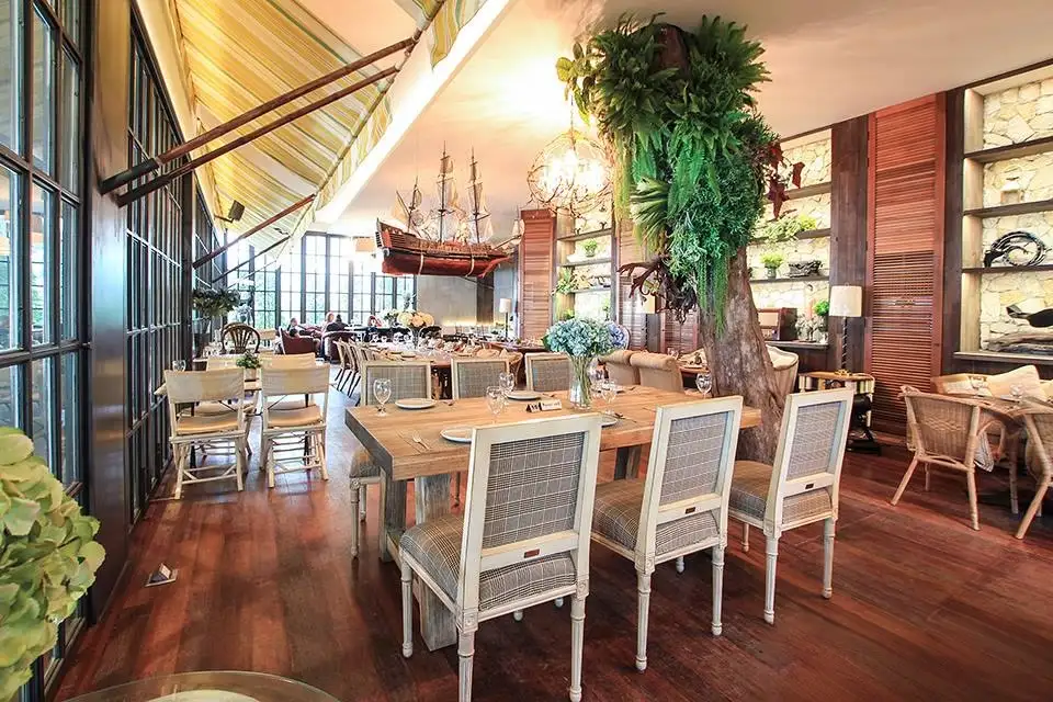 Family Trip in Pattaya: Beautiful dining room at The Glass House showcasing nautical elements, wooden furniture, and abundant greenery under soaring glass ceilings