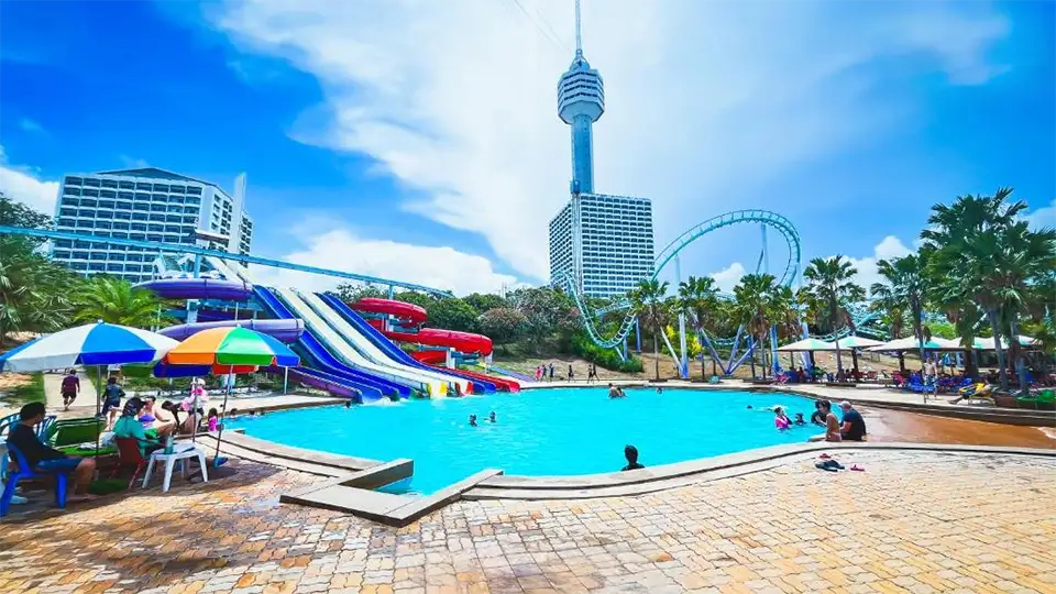 Family Trip in Pattaya: Colorful water slides and swimming pool at Pattaya Park Tower & Amusement Zone with the famous observation tower and roller coaster creating an exciting backdrop
