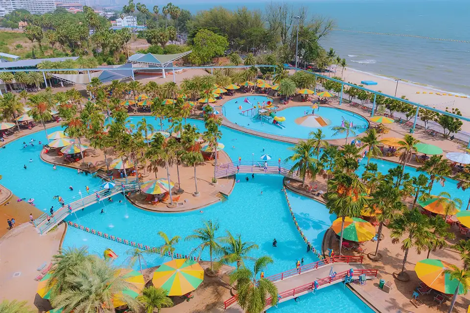 Family Trip in Pattaya: Overview of Pattaya Park's impressive aquatic facilities featuring multiple pools, palm trees, and colorful umbrellas with the Gulf of Thailand coastline visible.