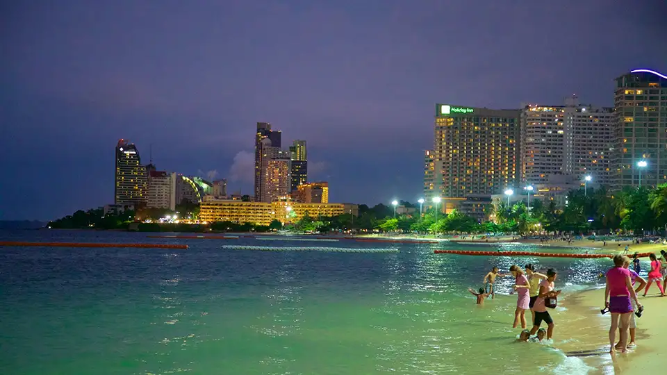 Family Trip in Pattaya: Families enjoying evening time at Pattaya Beach with kids playing in the shallow water and city lights in the background