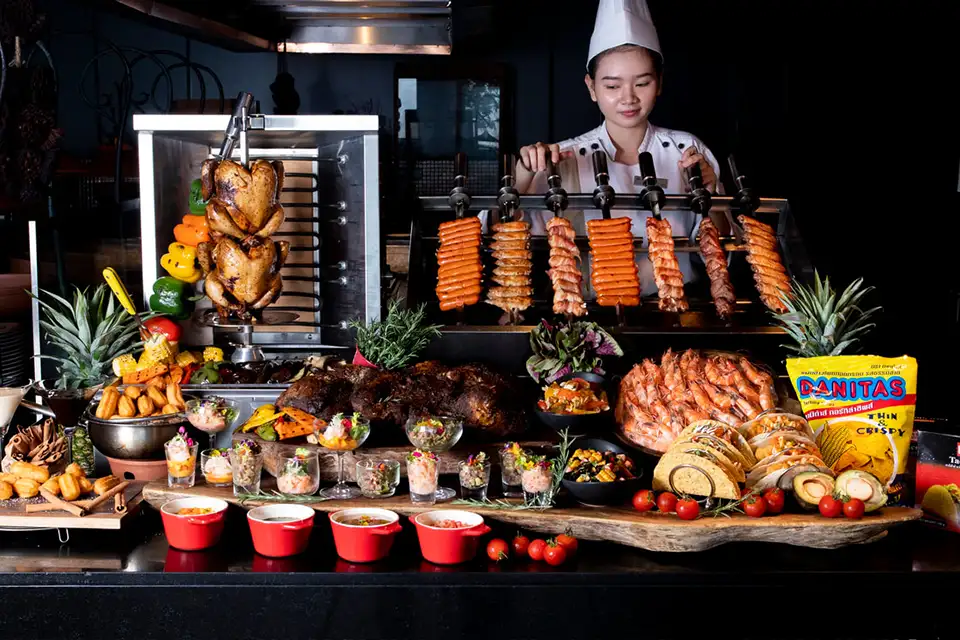 Family Trip in Pattaya: Chef preparing fresh grilled seafood and meats at a hotel buffet station with an elaborate spread of international dishes