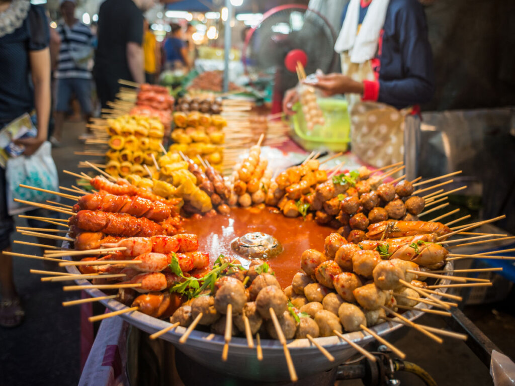 Family Trip in Pattaya: Local street vendor cooking assorted grilled skewers and hot pot dishes, perfect for families to try authentic Thai flavors