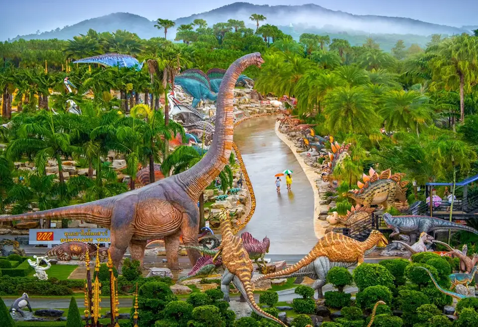 Dinosaur sculptures and tropical landscaping at Nong Nooch Tropical Garden in Pattaya, featuring life-sized prehistoric models among lush palm trees and mountain views