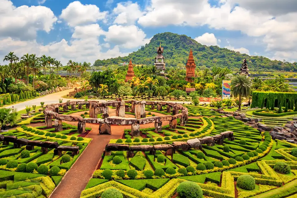 Elaborate formal gardens and Stonehenge replica at Nong Nooch Tropical Garden, featuring intricate topiary designs and manicured landscapes with mountains in the background