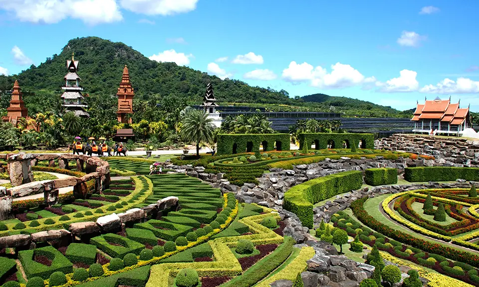 Pattaya photo spots: Stunning French-style formal gardens at Nong Nooch featuring intricate hedge mazes, colorful flower patterns, and traditional Thai architecture in the background