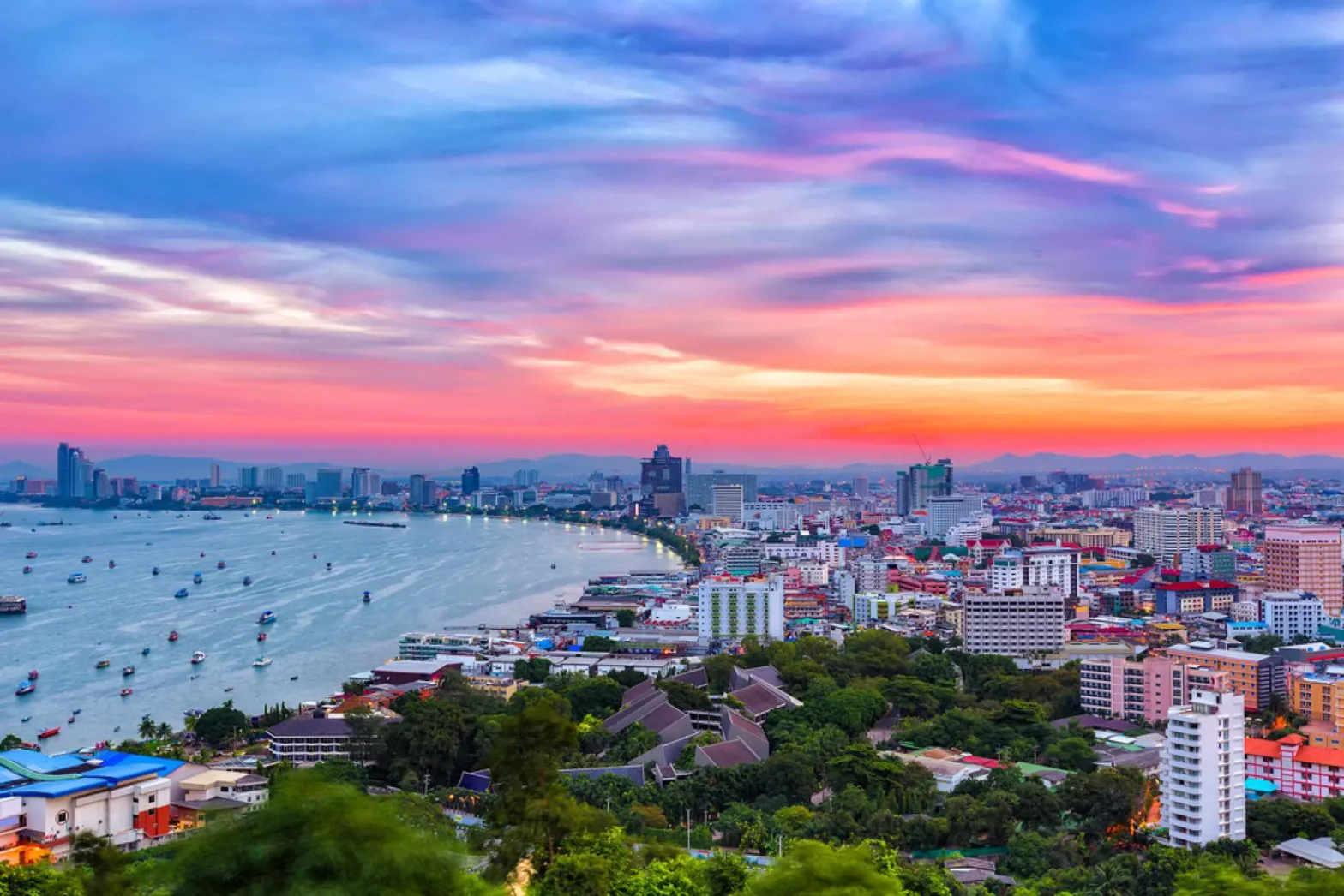 Stunning sunset view over Pattaya Bay with vibrant pink and orange clouds painting the sky above the bustling beachfront city and harbor filled with boats