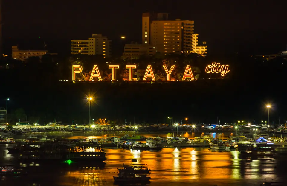 Night view of Pattaya City sign glowing above the bay, with boats reflecting on the water.