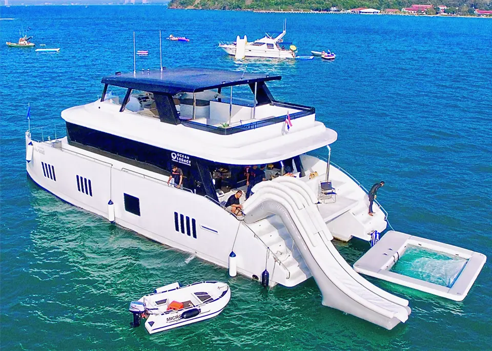 Modern white catamaran featuring an inflatable water slide and swimming platform anchored in the turquoise waters of Pattaya