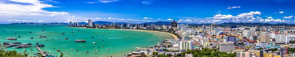 Panoramic view of Pattaya Bay with turquoise sea, boats, and city skyline under a bright blue sky.