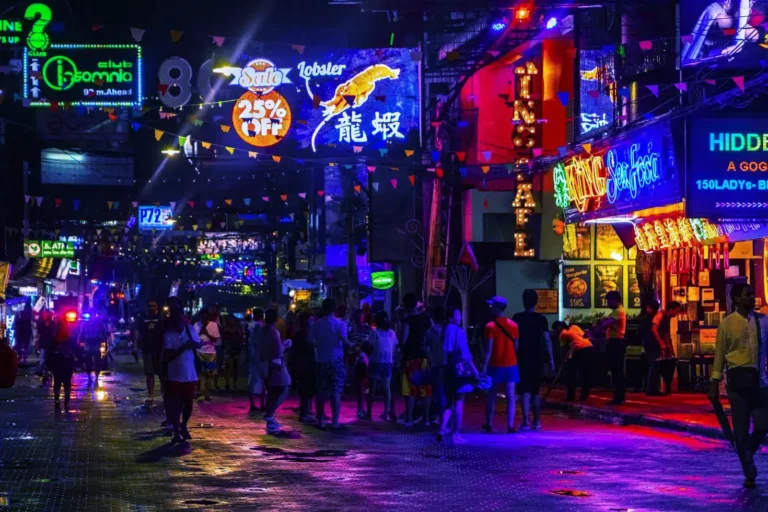 Lively evening atmosphere on Pattaya's famous Walking Street featuring bright neon signage in multiple languages, street vendors, and visitors exploring the bustling entertainment district