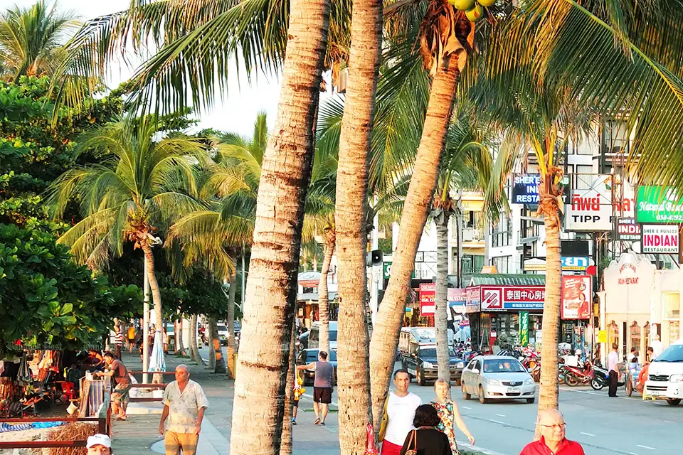 Tropical daytime street scene in Pattaya featuring swaying palm trees, colorful shop signs, and visitors exploring the area before the evening nightlife begins
