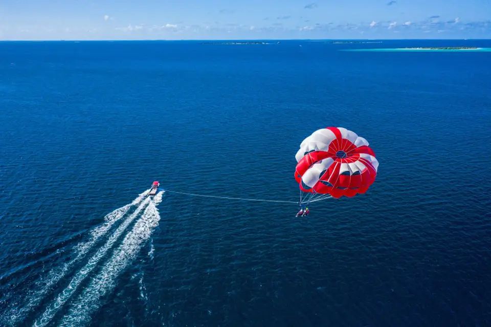 Aerial view of parasailing adventure with red and white parachute over deep blue waters near Pattaya