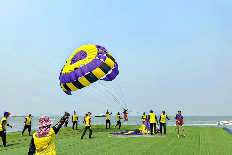 Parasailing operators setting up colorful parachute equipment as customers prepare for their water adventure