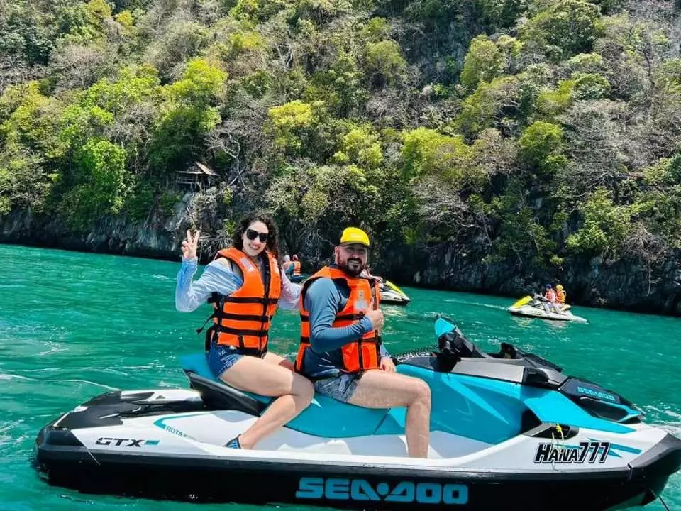 Couple having fun on jet ski adventure in crystal clear lagoon with dramatic limestone cliffs and green forest backdrop