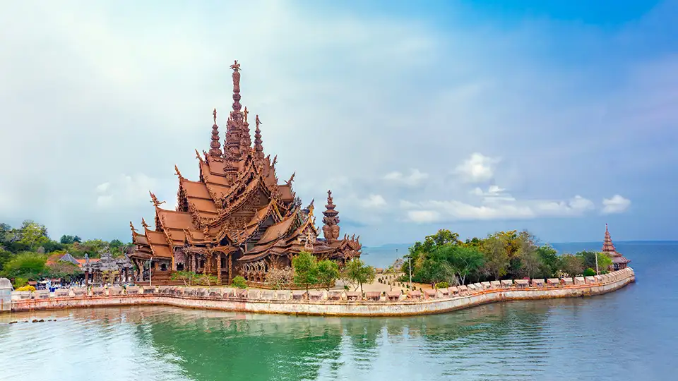 The Sanctuary of Truth wooden temple in Pattaya sits majestically on the waterfront, showcasing intricate Thai architecture against a blue sky