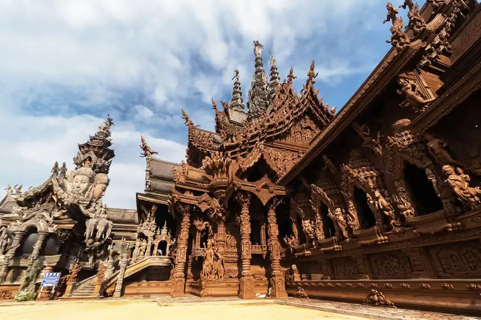 Detailed wooden architecture of the Sanctuary of Truth in Pattaya, showing elaborate carved spires and traditional Thai temple design against a cloudy sky