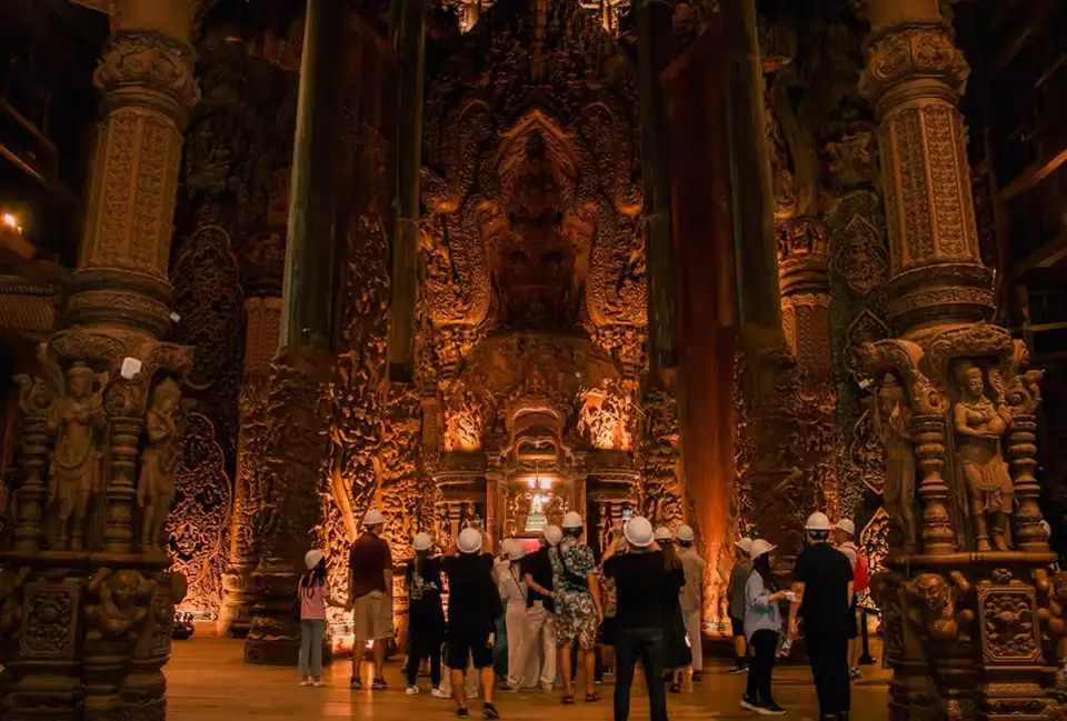 Tourists admiring the grand interior hall of the Sanctuary of Truth in Pattaya, surrounded by towering carved wooden columns and intricate religious sculptures