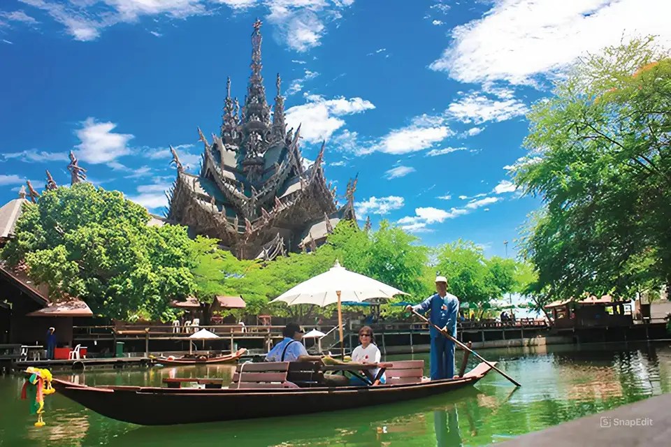 Traditional wooden boat ride at the Sanctuary of Truth in Pattaya, with the magnificent temple rising behind lush green trees under a bright blue sky