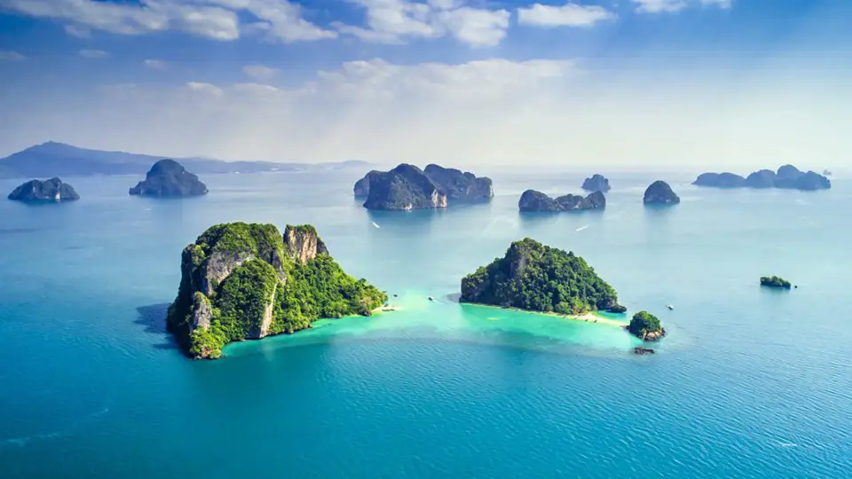 Stunning aerial panorama of Phang Nga Bay's iconic limestone islands scattered across calm blue waters, with a hidden lagoon nestled between jungle-covered karsts