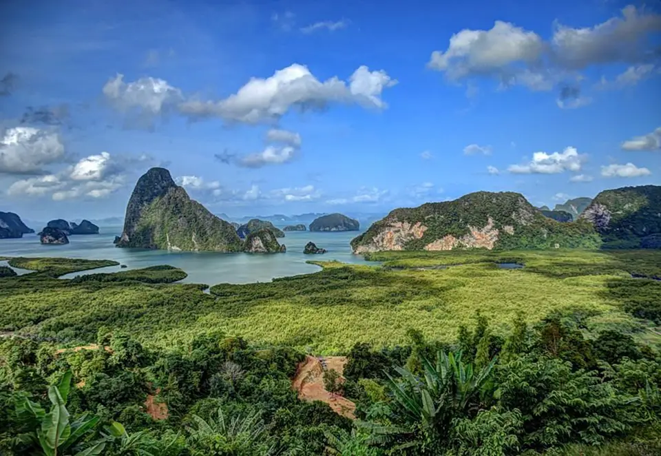 Panoramic view of Phang Nga Bay from a lush hilltop, showcasing dramatic limestone peaks rising from emerald waters amid dense tropical vegetation