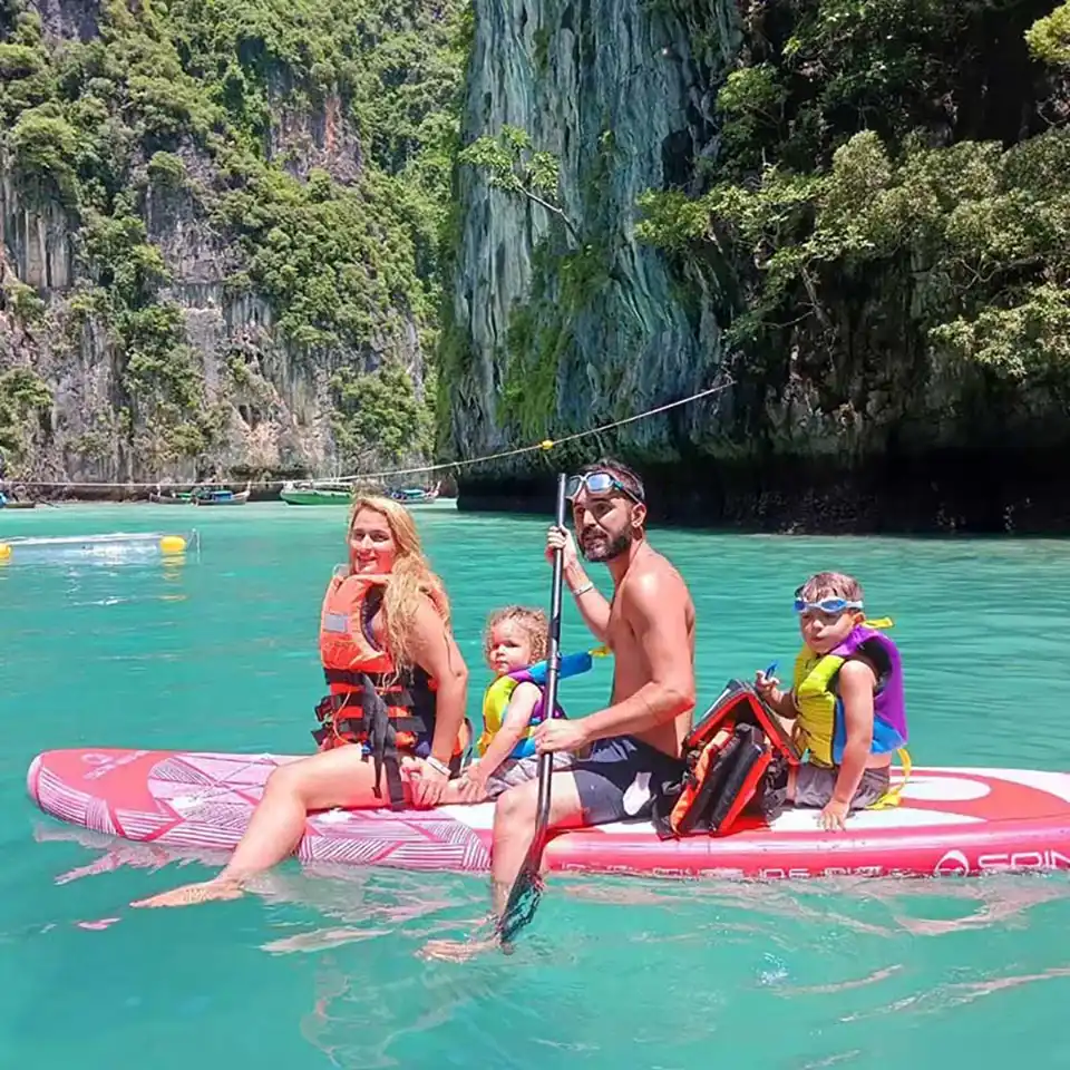 Phuket to Phi Phi Island Family of four enjoying a paddleboard in turquoise waters with dramatic limestone cliffs and lush tropical vegetation in the background