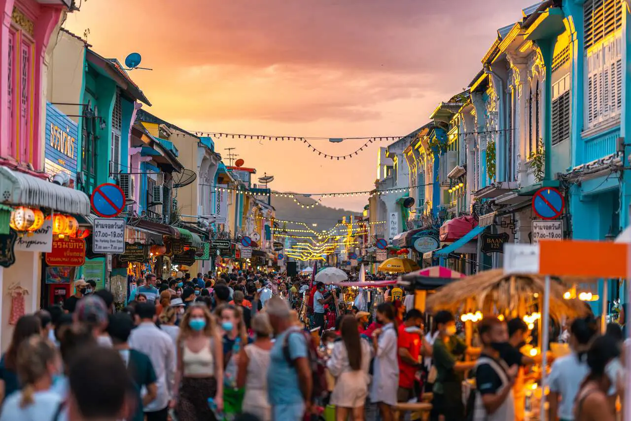 Lively night market in Phuket's old town featuring traditional Sino-Portuguese architecture, crowded with visitors browsing shops and food stalls under decorative string lights at golden hour