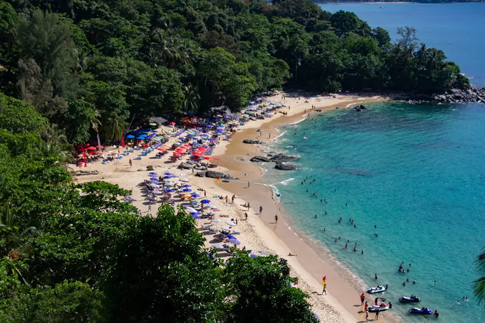 Hidden Beaches in Phuket: Aerial view of Laem Singh Beach in Phuket with colorful umbrellas, swimmers, and turquoise water.