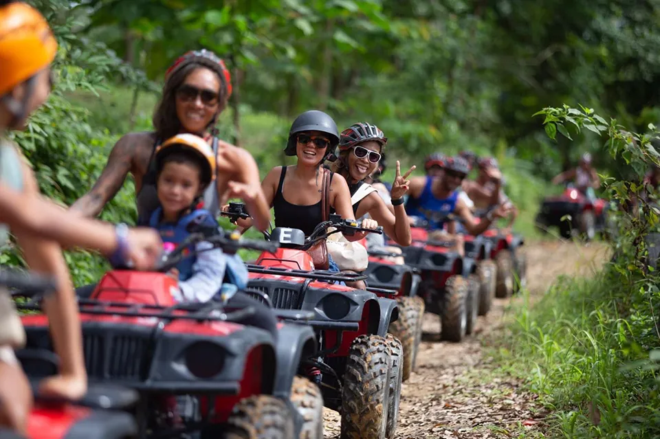 Phuket Family Trip: Families enjoying an exciting ATV buggy adventure through Phuket's jungle trails, riding red all-terrain vehicles in a convoy while exploring the island's tropical wilderness.