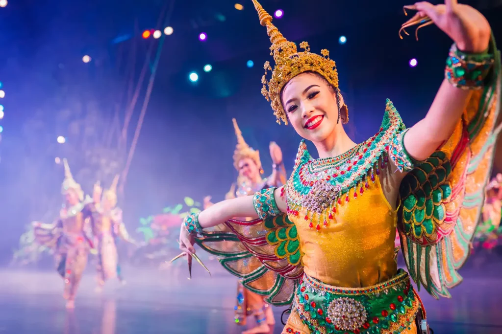 Phuket Cultural Shows: Smiling performer in ornate Thai traditional costume with golden headdress and colorful wings dances on stage at Phuket FantaSea
